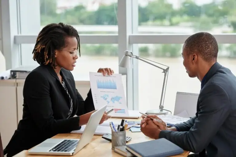 Two professionals in business attire reviewing documents during a meeting.